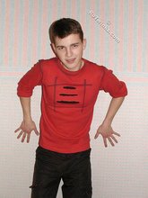 Brown-eyed young boy posing shirtless next to a wall