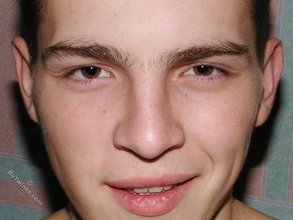 Brown-eyed young boy posing shirtless next to a wall