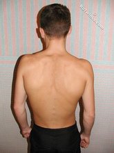 Brown-eyed young boy posing shirtless next to a wall