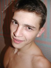 Brown-eyed young boy posing shirtless next to a wall