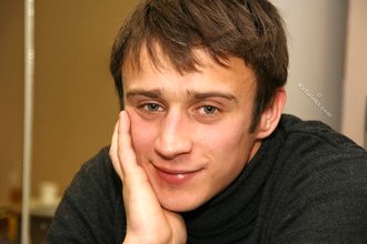 Dark-haired dude with beautiful eyes poses in his room