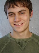 Smiling twink shows his hairy cock while resting on a bed