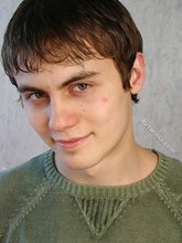 Smiling twink shows his hairy cock while resting on a bed