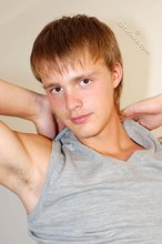 Blond-haired boy smiles at the camera while stripping for you