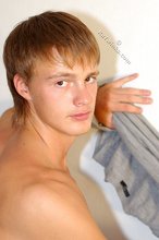 Blond-haired boy smiles at the camera while stripping for you
