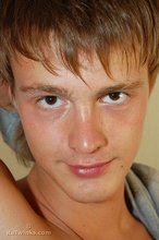 Blond-haired boy smiles at the camera while stripping for you