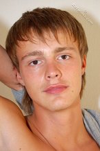 Blond-haired boy smiles at the camera while stripping for you
